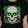 Gothic illustration of a detailed skull with electric green glowing eyes, surrounded by cannabis leaves and red roses on a black background. Gothic font text below reads: Hail The Herb. High-quality PNG for digital printing and merchandise.